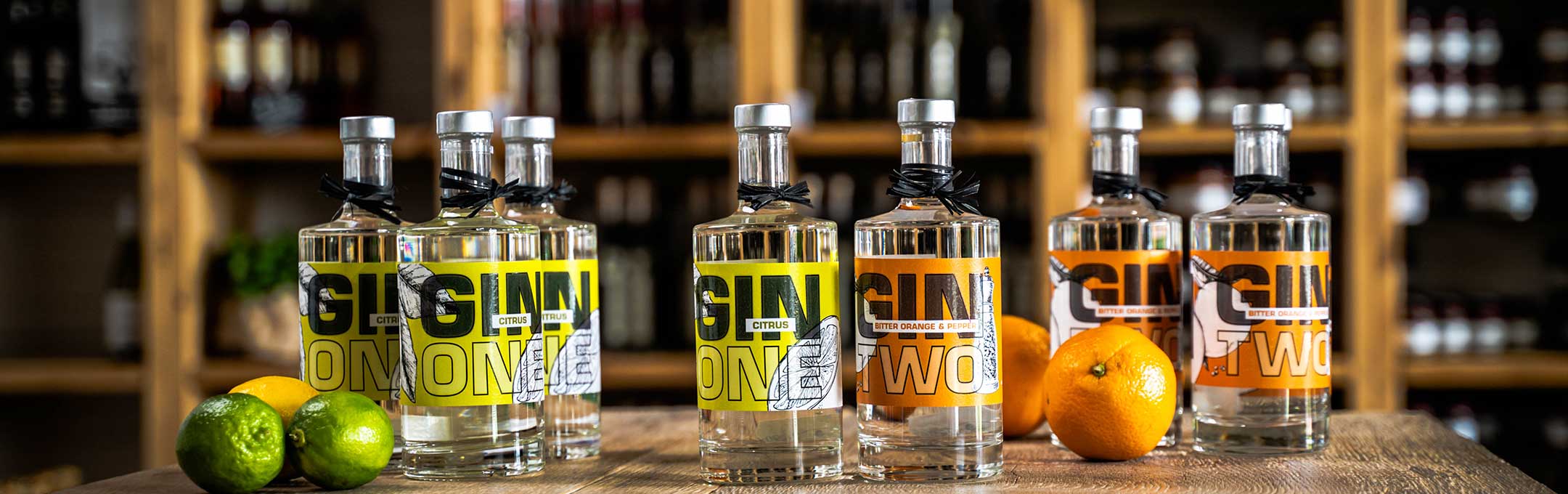 Mehrere Flaschen Gin, also besondere Spirituosen, mit einem Weinregal im Hintergrund.